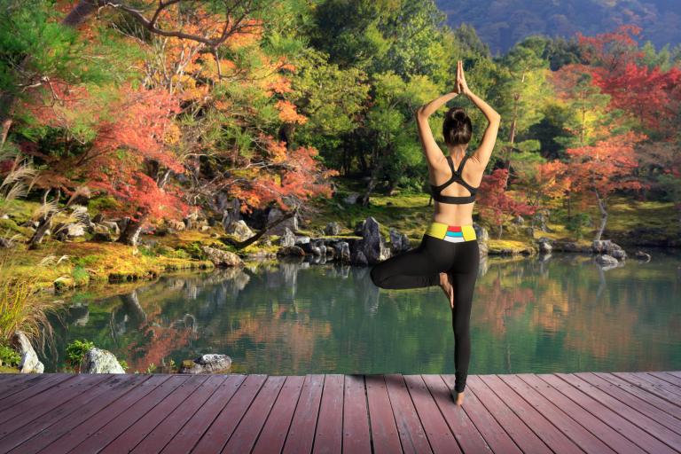 Woman in work out clothes doing tree pose on the dock of a pond during fall. 