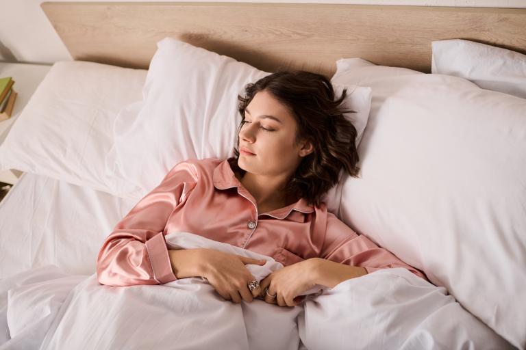 Woman in light pink pjs sleeps in bed.